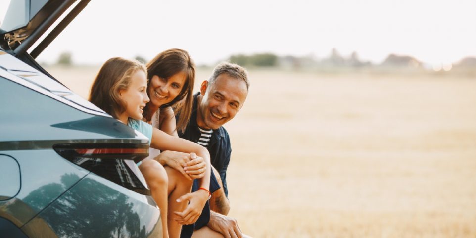 Family are sitting together in the car trunk and smiling and going to travel