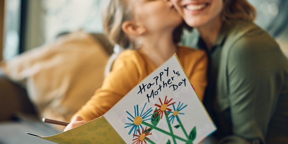 Close-up of woman receiving greeting card from her daughter on Mother's day, one of the fun ideas for Mothers day.