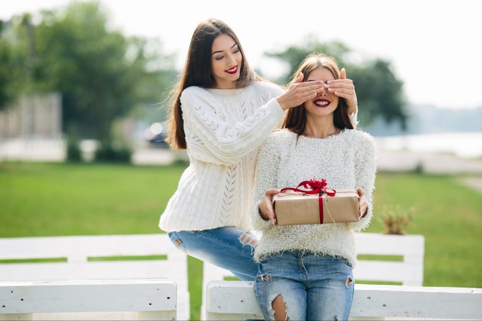 girl closes eyes with her hands the other girl with a gift