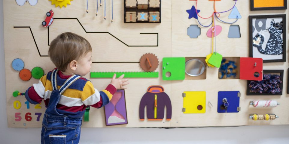 One year old boy playing on the busy board at psychotherapy office.