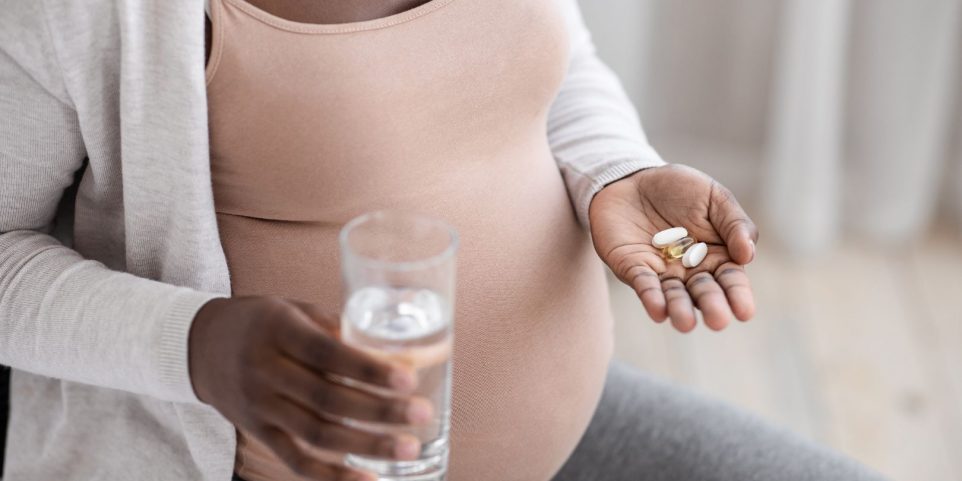 Prenatal Vitamins And Supplements. Unrecognizable black pregnant woman taking pills and water